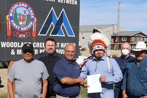 Mitarbeiter von Mercer und Woodland Cree First Nation stehen vor einem großen Peace River Logging Schild und halten gemeinsam einen Vertrag in der Hand.