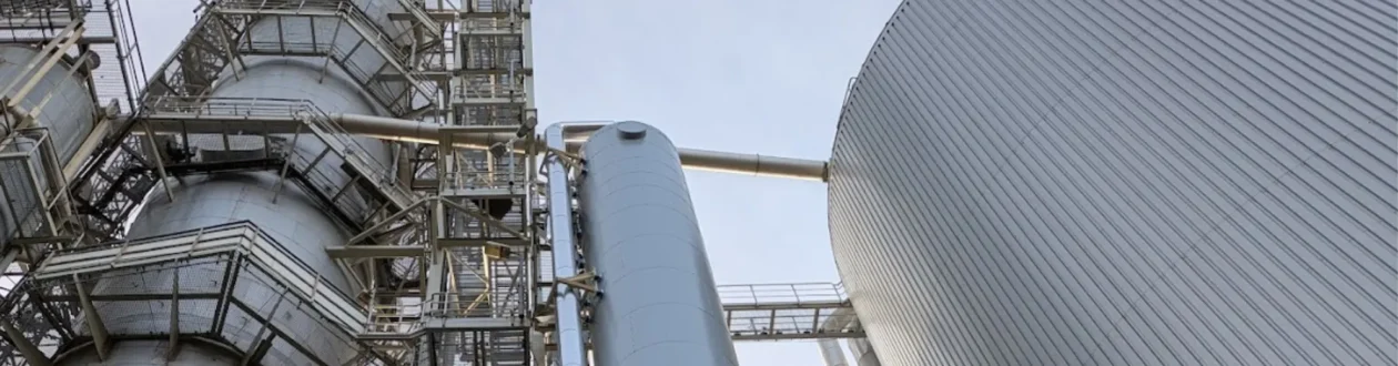 Industrieanlage: Silberne Tanks, Zylinder, Rohre und Gerüste dominieren das Bild, dazu ein großes, geripptes Gebäude.